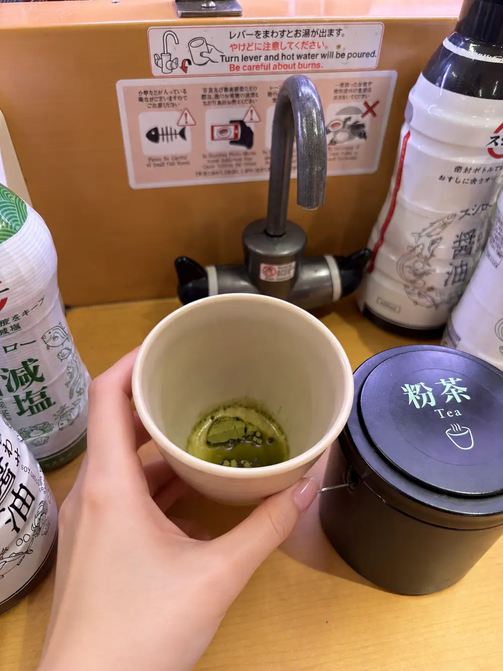 Powdered green tea cup and hot-water tap at a Sushiro seat